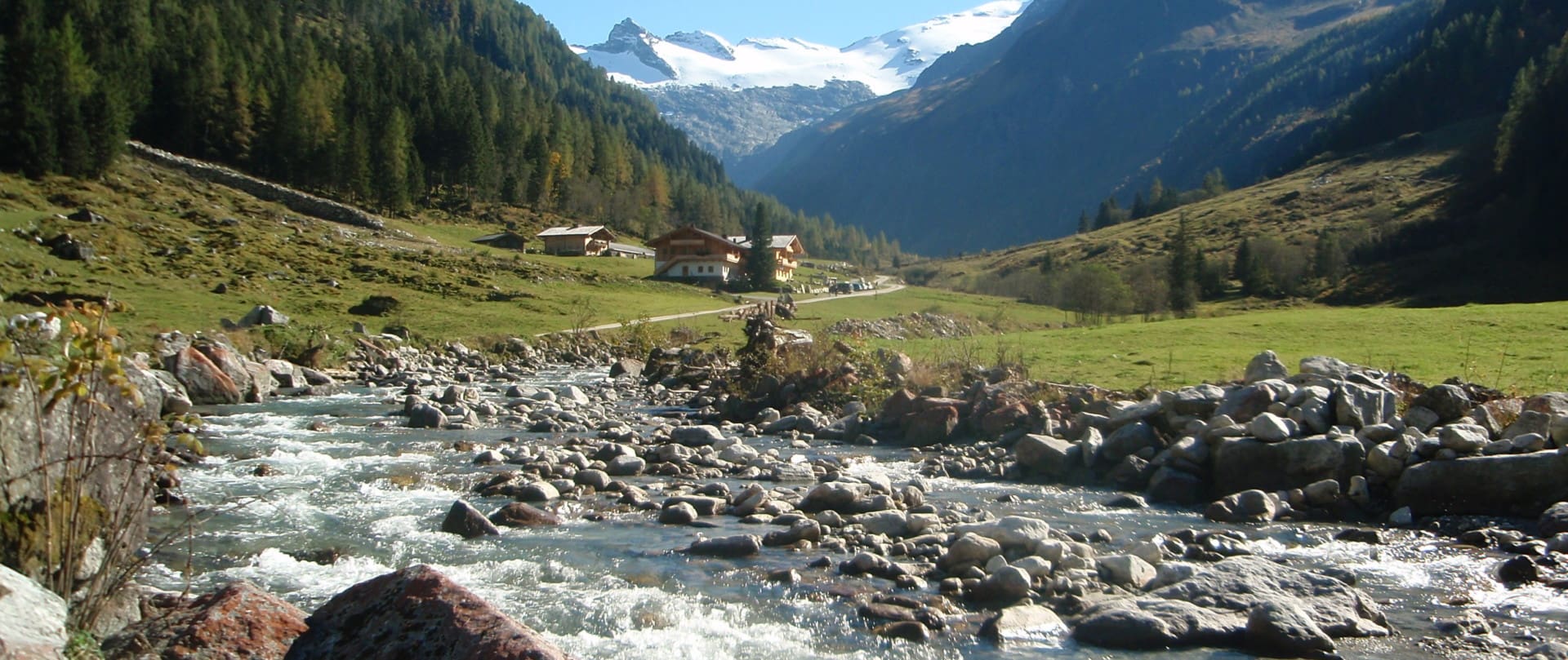 Gebirgsbach vor traditionellen Gasthof mit bergiger Landschaft im Hintergrund
